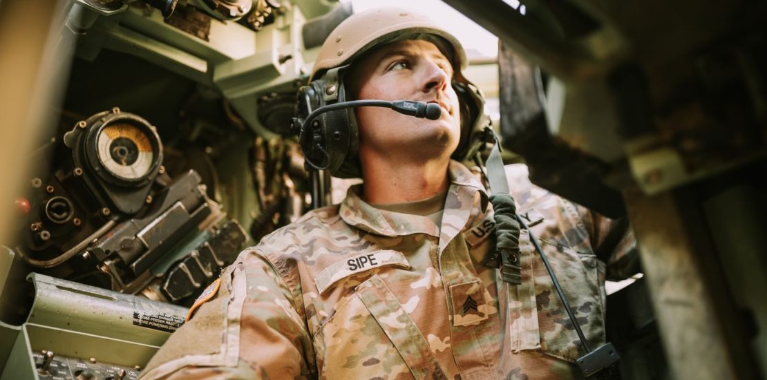 Photo by Art Guzman A soldier in camouflage uniform inside an armored vehicle, looking focused.